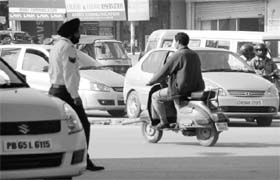 A traffic cop looks on as a helmet-less scooterist drives past him at Zirakpur on Thursday