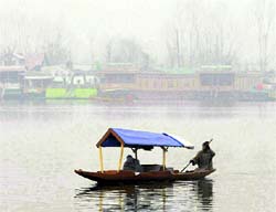 A boatman rows his boat amid fog on the Dal Lake