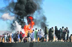 People stand along the wall of a truck terminal where fuel tankers were set ablaze in Quetta