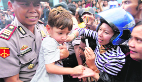 An Indonesian policeman carries a young survivor in Watulimo on Sunday.