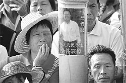 Residents of the Wukan village stand next to a poster showing local man Xue Jinbo, who died in police custody, during a town meeting
