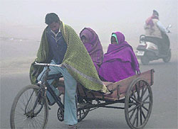 A man pedals a tricycle carrying two women during a cold and foggy morning in Gurgaon