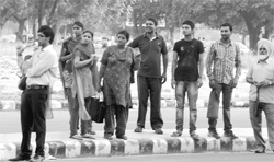 In the absence of a bus queue shelter, residents wait for a bus under scorching sun on the road separating Phases VII and VIII in Mohali.