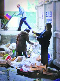 Two women collect food waste beside an industrial dumpster at the main food market in Madrid