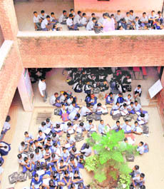 Students sit cramped in the open at a school.