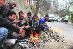 People sit around a bonfire on a cloudy morning in Shimla on Wednesday