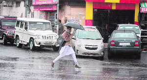 A man dashes across the road under the cover of an umbrella in Jammu, which received the first rainfall of the year on Friday. 