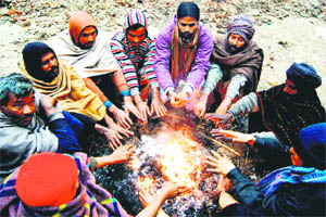 People sit by a bonfire to keep themselves warm on a chilly day in Amritsar on Saturday.  