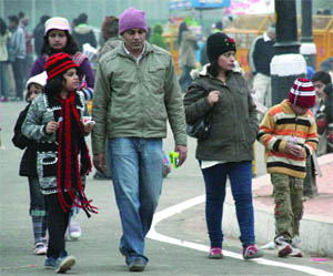 People cover themselves to save from the chilly wind as they walk on the road in New Delhi on Sunday. 