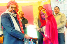 Jaiveer Singh, chief parliamentary secretary, gives the registry of a 100-square yard residential plot to an eligible woman at Rathdhana village on Monday. 