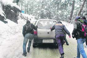 A policeman helps people push a vehicle on a slippery road after a snowfall in Shimla on Tuesday