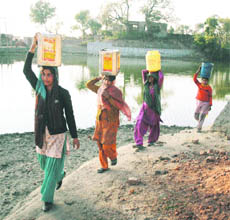 Women carry water on their heads from a nearby pond at Deon village in Samba district.