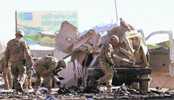A US soldier with the NATO-led International Security Assistance Force, looks for evidence as others walk at the sight of a suicide attack in Kandahar