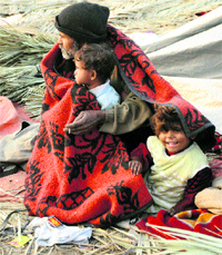 A roadside broom-maker and his children huddle together under a blanket on a cold day in Karnal.
