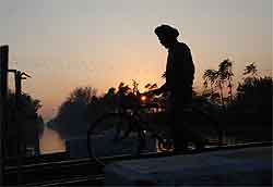 A man crossing the rail track over Sirhind canal is silhouetted against the setting sun in Bathinda