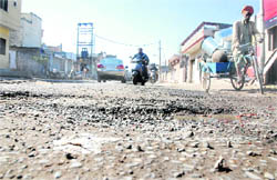 Motorists negotiate potholes on the damaged Jalandhar Cantonment-Garha Road in Jalandhar. 