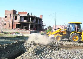 A bulldozer razes a road and other internal development works in an unauthorised colony on Chuharpur Road during a demolition drive in Ludhiana on Thursday
