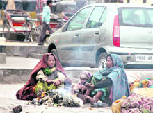 Poor women try to keep themselves warm by sitting around a bonfire after a drizzle in Jalandhar on Sunday. 