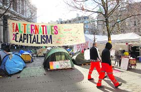 Workmen pass a sign that reads "There are alternatives to capitalism" at the Occupy London Stock Exchange demonstration in the early morning sunshine outside St. Paul's Cathedral in London on Saturday