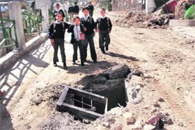 Schoolchildren walk past a damaged sewage chamber in Mussoorie