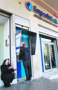 An old woman (L) begs as a man makes a transaction at an ATM outside an Emporiki Bank branch in Athens on Wednesday. Greece has received the first 7.5 bn euros ($9.9 bn) of aid from its new EU/IMF bailout. 