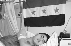A wounded Syrian youth lies under a pre-Baath Syrian flag, adopted by the anti-regime opposition, in Lebanon, where scores of Syrians have been receiving treatment.