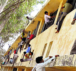 Perched precariously on windows, people help examinees by throwing slips inside an examination centre at Chang village of Bhiwani