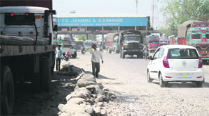 Vehicles pass through the damaged road at the gateway of Jammu-Lakhanpur toll plaza in Kathua.