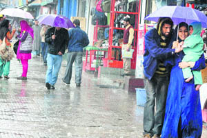 People huddle under umbrellas in a street in Srinagar on Wednesday.