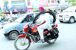 A man carries pipe on his shoulder while driving his motorcycle on a busy road in Bathinda. 