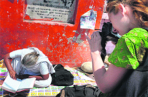 A foreigner clicks a photograph of an old woman reading the Ramayana near the Ganga ghat in Haridwar. 