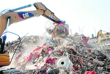 Blankets lie strewn around as a JCB machine clears debris at the disaster site.