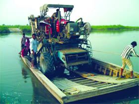 Farmers having land holdings across the Sutlej using a boat to ferry a harvesting machine to their fields, in Ferozepur district. 