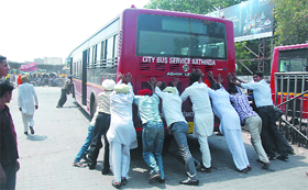 People push the newly launched city bus that broke down near the bus stand on Sunday.