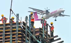 Construction workers erect scaffolding at the site of a metro station as an aircraft flies past in Chennai on Monday. Growth in Asia's third-largest economy is slowing as costlier credit and the impact of Europe's debt crisis on exports have sapped expansion. Indias GDP rose 6.1% in the December quarter from a year earlier, the slowest pace in near three years. 