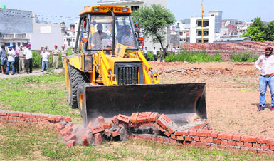 A low-height boundary wall being demolished by the Nayagaon NAC on Monday in wake of the Punjab and Haryana High Court order on the catchment area.