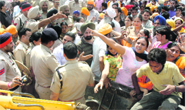 Protesters lie in front of a earth moving machine as the teams of the MC and the JIT try to remove illegal structures in Guu Teg Bahadur Nagar in Jalandhar on Monday.
