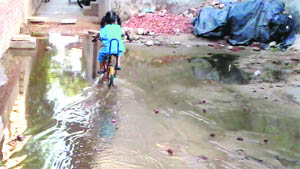A child on bicycle crosses a street flooded with filthy water at Anil Nagar in Jagraon