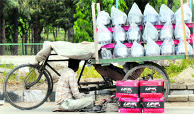 A roadside helmet-seller uses his cart as a shield against the scorching sun in Karnal on Friday.
