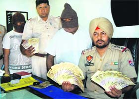 The police shows the fake currency notes recovered from two persons, standing with faces covered, in Jalandhar on Tuesday