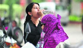 A girl quenches her thirst with water while another has covered her head with a scarf to save herself from the sun
