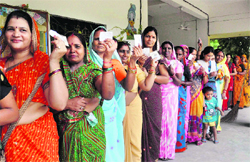 Women show their voter ID cards as they stand in queue at a polling station in Lucknow on Saturday.  PTI