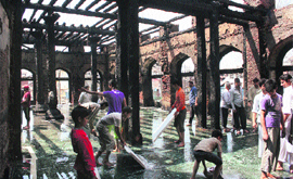 Locals along with the fire and emergency services personnel clean the gutted shrine of Dastageer Sahab on Tuesday. 