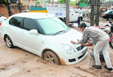 People push a car stuck in mud at the tehsil complex parking in Dera Bassi. 
