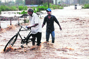 A man struggles with his cycle as he crosses a flooded road at Zirakpur on Saturday.
