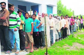 Voters wait outside a polling booth to cast their votes in the Sitarganj bypoll in Udham Singh Nagar on Sunday