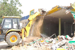 A JCB machine razes a building constructed on a government land on the national highway in Gidderbaha on Wednesday. 