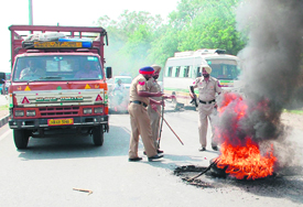 Policemen try to remove the tyres, which were set afire by an agitating mob, on the national highway at Jandiala Guru near Amritsar on Wednesday.