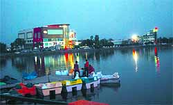 A boat is being readied for sail in the Thermal lake at dusk with illuminated business establishments in the backdrop. The area has undergone a sea-change with recreational facilities coming up to attract visitors