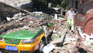 A resident walks past debris and a taxi damaged by floods after heavy rainfall in Mentougou district of Beijing on Sunday.